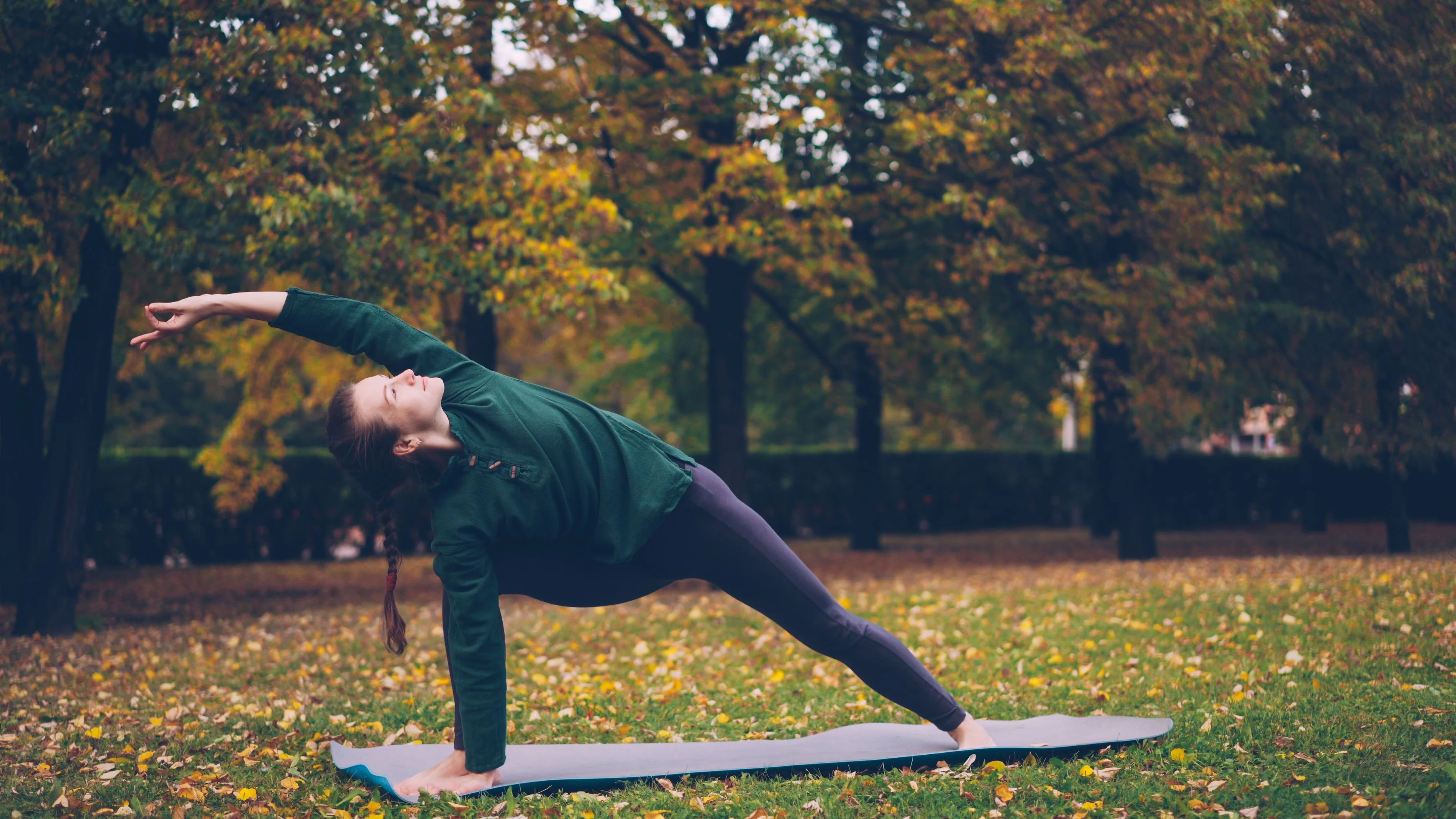 Woman holding a side angle pose in an autumn park